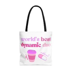 Può includere: Borsa tote bianca con manici neri. La borsa ha testo rosa e viola che dice "world's best dynamic duo" con un cuore rosa tra le parole. C'è una tazza di caffè rosa con la parola "coffee" scritta su di essa e una pillola rosa con la parola "adderall" scritta su di essa.