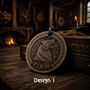 Könnte beinhalten: Ein kreisförmiger, bronzefarbener Metallanhänger mit einem Relief eines heulenden Wolfskopfes in der Mitte. Das Design enthält eingravierte Runensymbole an den Seiten und den Namen FINN am unteren Rand. Ein Metallring ist oben befestigt.
