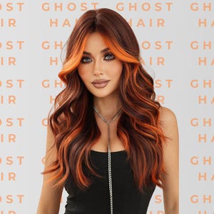 May include: A woman with long, wavy auburn hair with bright orange highlights. The hair is styled with a side part and falls over the shoulders. The background has the words "GHOST HAIR" repeated in a pattern. She wears a black top and a silver necklace.