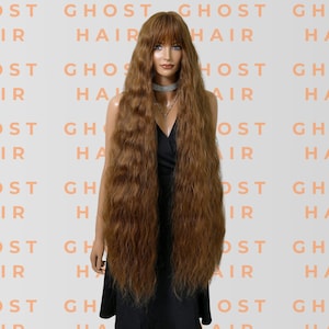 May include: A mannequin displays a long, auburn wig with a fringe. The wig has a wavy texture and falls well below the waist. The background is patterned with the words "GHOST HAIR" in a light orange hue.