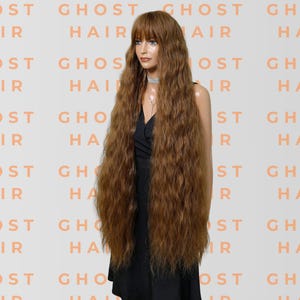 May include: A long, wavy auburn wig with a fringe is displayed on a mannequin. The wig is styled with voluminous, crimped waves. The background features the words "GHOST HAIR" in a repeating pattern.