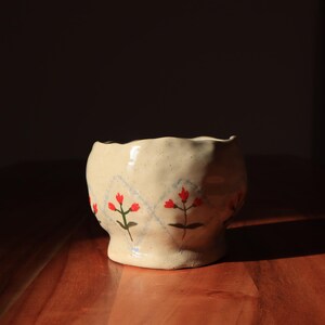 May include: A cream-coloured ceramic bowl with a wavy rim and a floral design. The bowl has a blue and white diamond pattern with red flowers.