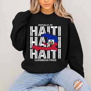 Può includere: Felpa nera con la scritta bianca "REPUBLIC OF HAITI", impilata verticalmente, con una mappa di Haiti in rosso, blu e verde. Il testo "CARIBBEAN PRIDE" è sotto la parola "HAITI".