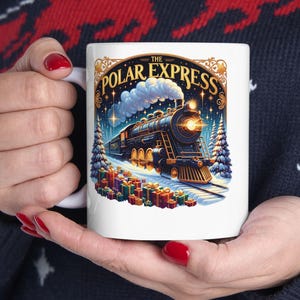 Könnte beinhalten: Weiße Keramiktasse mit einer detaillierten Illustration eines alten Zuges, schneebedeckten Bäumen und verpackten Geschenken. Die Tasse trägt den Text "The Polar Express" in einer dekorativen Schriftart und erinnert an ein festliches Urlaubsthema.
