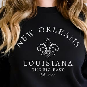 Show off your love for the soul of the South with this stylish New Orleans Sweathirt featuring a minimalist fleur-de-lis and elegant vintage-style typography. Inspired by the cultural richness of Louisiana, this shirt pays tribute to "The Big Easy" and its founding in 1718.
