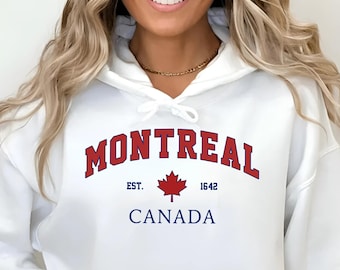 May include: White hooded sweatshirt with the word "MONTREAL" in red arched lettering. Below the word "MONTREAL" is a red maple leaf and the words "EST. 1642 CANADA" in blue. The sweatshirt has a front pocket and a drawstring hood.