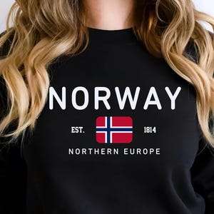 Puede incluir: Sudadera negra con la palabra "NORWAY" en letras blancas. Debajo, la bandera noruega, el texto "EST. 1814" y "NORTHERN EUROPE". La sudadera tiene mangas largas.