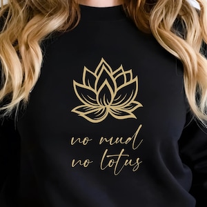 Peut inclure: Sweat-shirt noir avec un motif de fleur de lotus dorée et l'inscription "no mud no lotus". Le sweat-shirt à manches longues a un col rond. Le logo Atlas Dall Crafts est visible en haut à gauche.