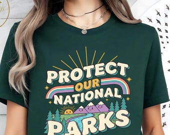 May include: Dark green t-shirt with the text "PROTECT OUR NATIONAL PARKS" in a retro design. The graphic includes a rainbow, mountains, trees, and a sun. The shirt is a crew neck style.