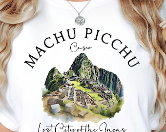 Puede incluir: Camiseta blanca con una ilustración de acuarela de Machu Picchu, con el texto "Machu Picchu Cusco" y "Lost City of the Incas PERU". Se sostiene un vaso con un diseño floral.