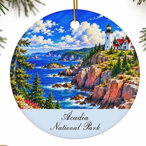 Peut inclure: Une décoration en céramique ronde illustrant un paysage peint d'un phare sur une falaise rocheuse surplombant l'océan. Le texte Acadia National Park est imprimé en écriture noire sur la partie inférieure du fond blanc.