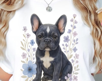 May include: White t-shirt with a watercolour illustration of a black French Bulldog, framed by blue and purple flowers. The shirt has the word "White" printed on the bottom right. The brand logo "Atlas Dali Crafts" is on the bottom left.