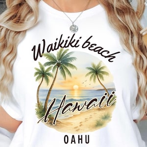 Peut inclure: T-shirt blanc avec un motif aquarelle représentant des palmiers, un coucher de soleil et les mots "Waikiki beach Hawaii Oahu". Le t-shirt a un col rond et des manches courtes. Un verre avec un motif floral est tenu dans la main.