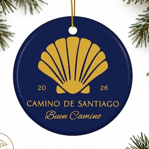 Peut inclure: Une décoration ronde en céramique bleu foncé avec un motif de coquille Saint-Jacques dorée au centre. Le texte 2026, CAMINO DE SANTIAGO et Buen Camino est imprimé en doré sous la coquille. Un cordon doré est fixé au sommet pour suspendre.