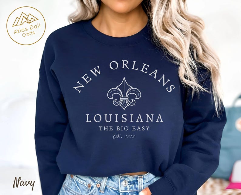 May include: Navy blue sweatshirt with white text and a fleur-de-lis design. The text reads "New Orleans Louisiana The Big Easy Est. 1718". The sweatshirt is a crew neck style.