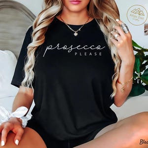 Peut inclure: T-shirt noir avec l'inscription blanche "prosecco PLEASE" en &eacute;criture cursive. Le t-shirt est de style col rond. On aper&ccedil;oit &eacute;galement un collier et un bracelet dor&eacute;s.