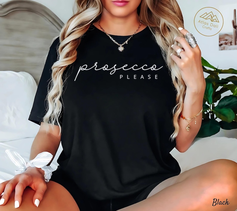 Peut inclure: T-shirt noir avec l'inscription blanche "prosecco PLEASE" en &eacute;criture cursive. Le t-shirt est de style col rond. On aper&ccedil;oit &eacute;galement un collier et un bracelet dor&eacute;s.