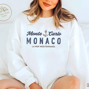 May include: White sweatshirt with the text "Monte Carlo Monaco" in navy blue, featuring an anchor graphic. Below the text is "La Mer M&eacute;diterran&eacute;e". The sweatshirt has a crew neck and long sleeves.