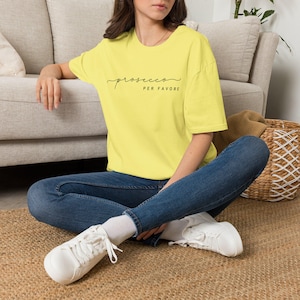 Op de afbeelding: Een felgeel T-shirt met korte mouwen en de zwarte tekst "prosecco PER FAVORE" op de borst. Het shirt heeft een ronde hals en een relaxte pasvorm, gecombineerd met een donkerblauwe spijkerbroek en witte sneakers met veters.