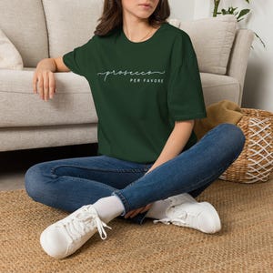 Op de afbeelding: Een donker bosgroen T-shirt met korte mouwen en de witte tekst "prosecco PER FAVORE" op de borst. Het shirt heeft een ronde hals en een relaxte pasvorm, gecombineerd met een blauwe spijkerbroek en witte sneakers met veters.