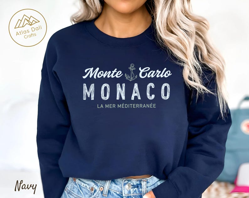 May include: Navy blue sweatshirt with the text "Monte Carlo MONACO" in white, along with an anchor graphic. The phrase "LA MER M&Eacute;DITERRAN&Eacute;E" is below the city name. The sweatshirt has a crew neck and long sleeves.