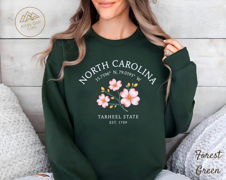 Op de afbeelding: Bostongroen sweatshirt met de tekst "NORTH CAROLINA" en co&ouml;rdinaten, plus een bloemenafbeelding. Daaronder staat "TARHEEL STATE EST. 1789". De sweatshirt is effen van kleur en heeft een ronde hals.