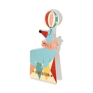 May include: A whimsical invitation card featuring a light blue seal balancing a striped ball on its nose. The seal is wearing a pink ruffled collar and is perched on a colorful geometric shape. The word "INVITATION" is printed on the card.