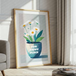May include: A framed art print depicting a vase of daisies with the text "OUR HAPPY PLACE". The blue vase holds daisies with white petals and yellow centres. The artwork is displayed in a room with a window and curtains.