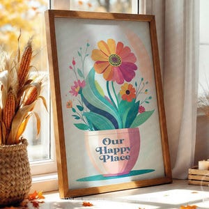 Könnte beinhalten: Gerahmter Kunstdruck mit einem farbenfrohen Blumenarrangement in einem rosa Topf mit dem Text "Our Happy Place". Das Kunstwerk enthält einen Regenbogen und befindet sich vor einem Fenster mit Herbstdekoration.