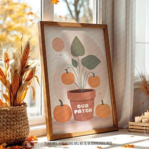 Puede incluir: Una impresión artística enmarcada que presenta una planta con calabazas en una maceta de terracota, con el texto "OUR PATCH". La obra de arte se encuentra sobre un fondo suave y neutro. La escena incluye una cesta tejida con mazorcas de maíz y una calabaza.