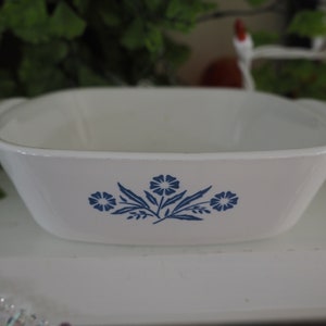 Puede incluir: Plato para hornear de cerámica blanca con diseño floral azul. El plato tiene dos asas a los lados.