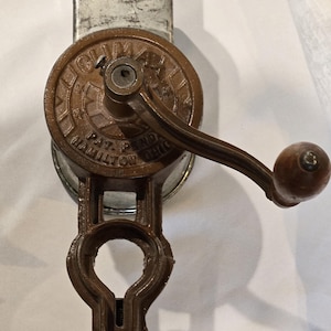 Puede incluir: Antigua máquina de afeitar hielo manual, en tonos marrón y plateado. La manivela redonda lleva la inscripción "CLIMAX" y "PAT. PEND. HAMILTON OHIO". El mango tiene un pomo de madera. Tiene una abrazadera para fijarla.