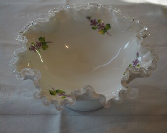 Puede incluir: Un tazón de vidrio blanco con un borde plateado y un delicado diseño floral con flores moradas y hojas verdes.