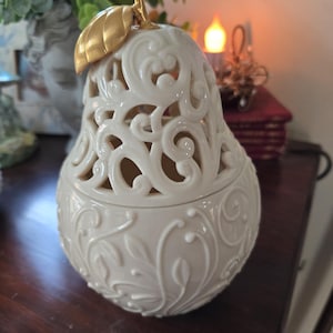 May include: A white porcelain pear-shaped candle holder with a gold leaf design. The holder has an intricate, cut-out pattern and is perfect for adding a touch of elegance to any home.