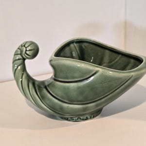 Può includere: Una fioriera vintage a forma di cornucopia in ceramica verde. La fioriera ha una finitura lucida e un design a forma di corno arricciato su un'estremità. La base è contrassegnata con "U.S.A. 271".