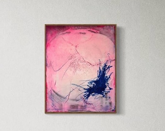 Op de afbeelding: Abstract kunstwerk met een roze en witte achtergrond en een vleugje blauwe verf. Het schilderij zit in een bruine lijst en hangt aan een witte muur. Een modern bureau met zilveren afwerking, een stoel en een open boek staan op de voorgrond.