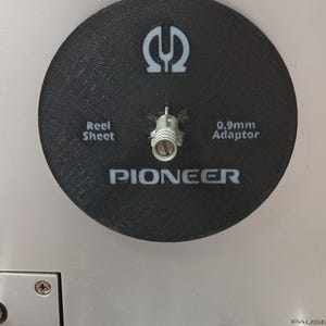 May include: A black circular Pioneer reel sheet with a 0.9mm adaptor. The reel sheet has the Pioneer logo and the text "Reel Sheet" and "0.9mm Adaptor" printed on it. The reel sheet is mounted on a silver surface.