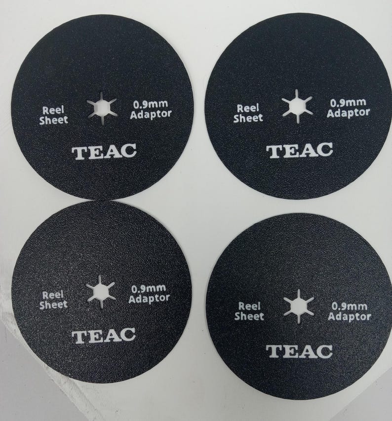 May include: Four black circular reel sheet adaptors. Each adaptor has the text "Reel Sheet", a star-shaped design, "0.9mm Adaptor", and the brand name "TEAC" in white text. The adaptors are designed for audio equipment.