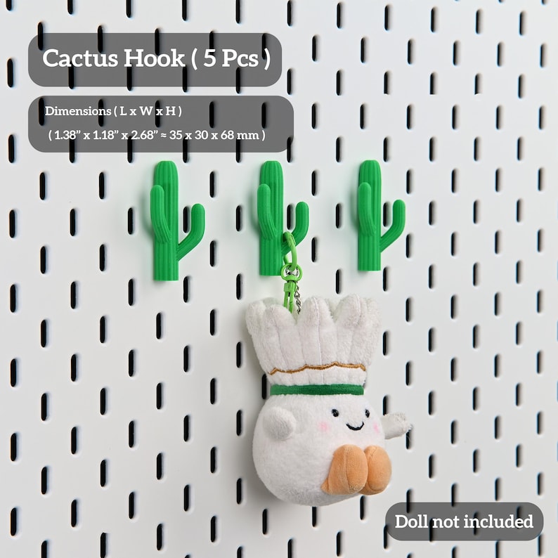 Puede incluir: Ganchos verdes con forma de cactus sobre una pared perforada blanca. Los ganchos miden aproximadamente 3,5 cm de largo, 3 cm de ancho y 6,8 cm de alto. El texto "Cactus Hook (5 Pcs)" es visible. Una mu&ntilde;eca de peluche cuelga de uno de los ganchos.