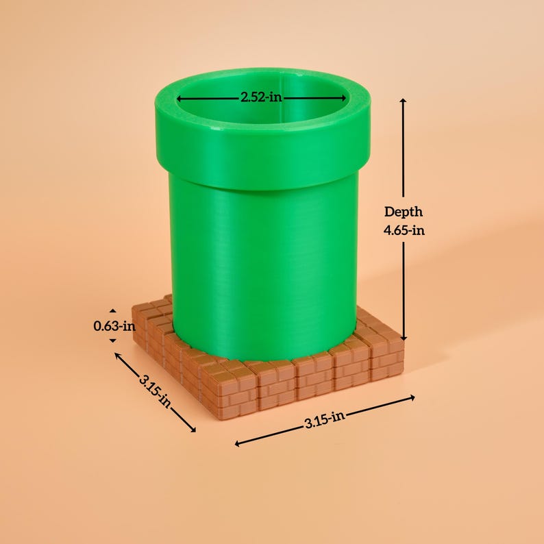 May include: A green pipe with a 6.4 cm diameter and a 11.8 cm depth, set on an 8 cm square brick base. The base is 1.6 cm thick. The pipe is a vibrant green colour, and the base is a brown brick colour.