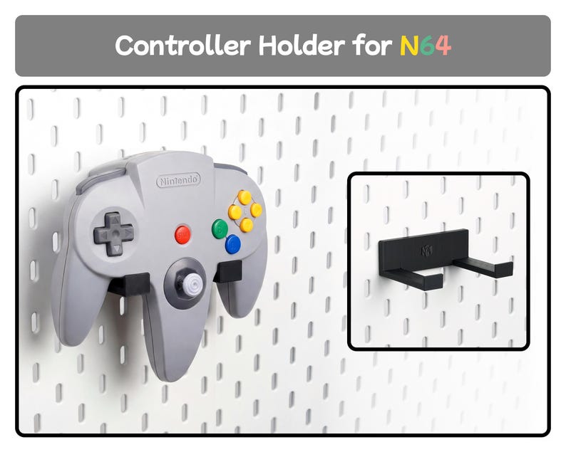 May include: A black plastic controller holder for N64 mounted on a white pegboard. The holder features two horizontal prongs to support a grey Nintendo 64 game controller. The text Controller Holder for N64 is displayed at the top of the image.