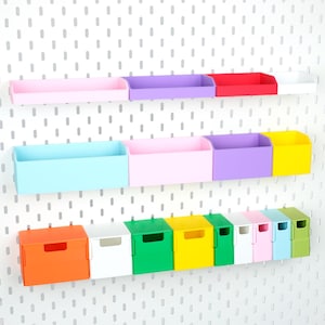 Puede incluir: Una colección de contenedores y cajas de almacenamiento de plástico de colores montados en un tablero perforado blanco. El conjunto incluye varias bandejas rectangulares y pequeñas cajas cuadradas en tonos rosa, morado, rojo, blanco, azul, amarillo, naranja y verde.