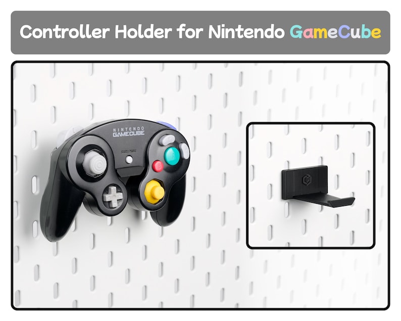 May include: A black plastic controller holder for a Nintendo GameCube console, designed to mount onto a white pegboard. The holder features a small embossed logo and is shown both empty and supporting a black Nintendo GameCube game controller.