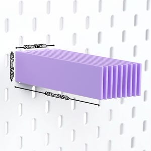 Puede incluir: Un estante de pl&aacute;stico de color morado claro para tablero perforado, con una serie de listones verticales. El estante mide 158 mm de largo, 59 mm de profundidad y 36,4 mm de alto, seg&uacute;n las etiquetas de dimensiones visibles en la imagen.