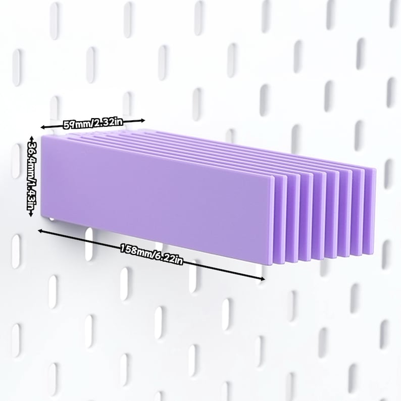 Puede incluir: Un estante de pl&aacute;stico de color morado claro para tablero perforado, con una serie de listones verticales. El estante mide 158 mm de largo, 59 mm de profundidad y 36,4 mm de alto, seg&uacute;n las etiquetas de dimensiones visibles en la imagen.