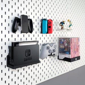 May include: A wall-mounted gaming console and accessories organizer. Includes a black console dock, controllers, and game cartridges. The accessories are in black, gray, red, and blue. The wall is white with evenly spaced holes.