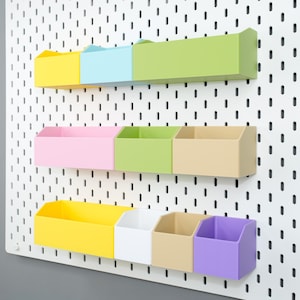 Può includere: Un set di contenitori portaoggetti multicolore da parete in giallo, azzurro, verde, rosa, bianco, beige e viola. I contenitori sono fissati a una pannello forato bianco con fori distanziati, offrendo una soluzione organizzativa moderna.