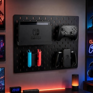 Peut inclure: Organisateur de pegboard noir avec une console Nintendo Switch, des manettes et des accessoires. Le tableau comporte une grille de trous pour le montage d'articles. Une manette Pro noire et des Joy-Cons bleus et rouges sont visibles.