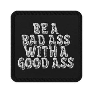 Può includere: Toppa quadrata nera con testo ricamato bianco: "BE A BAD ASS WITH A GOOD ASS". La toppa ha un bordo nero ed è progettata per essere cucita o stirata su abbigliamento o accessori.
