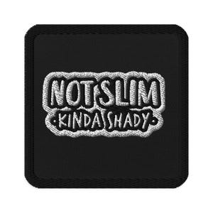 May include: Black square patch with white embroidered text that reads "NOT SLIM KINDA SHADY". The patch has a black border and is likely designed to be sewn or ironed onto clothing or accessories.